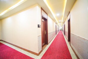Un couloir d’hôtel avec un tapis rouge, des portes en bois et un panneau indiquant les numéros de chambre.