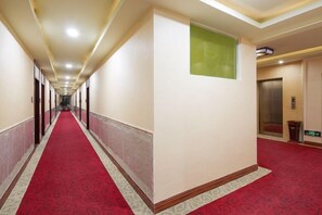 A hotel corridor with a red carpet, a green window, and an elevator.