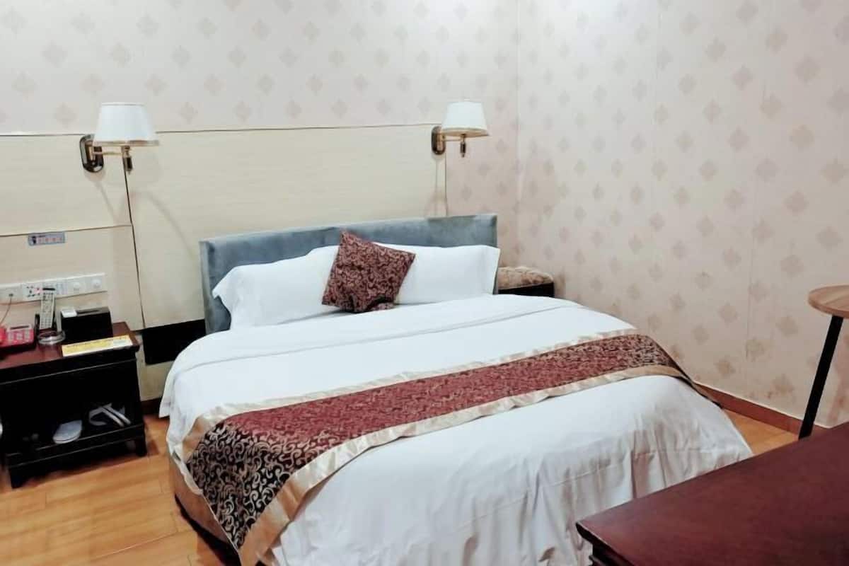 Ein ordentlich eingerichtetes Hotelzimmer mit einem Bett, Nachttischen, Lampen und einem kleinen Schreibtisch mit Stuhl.