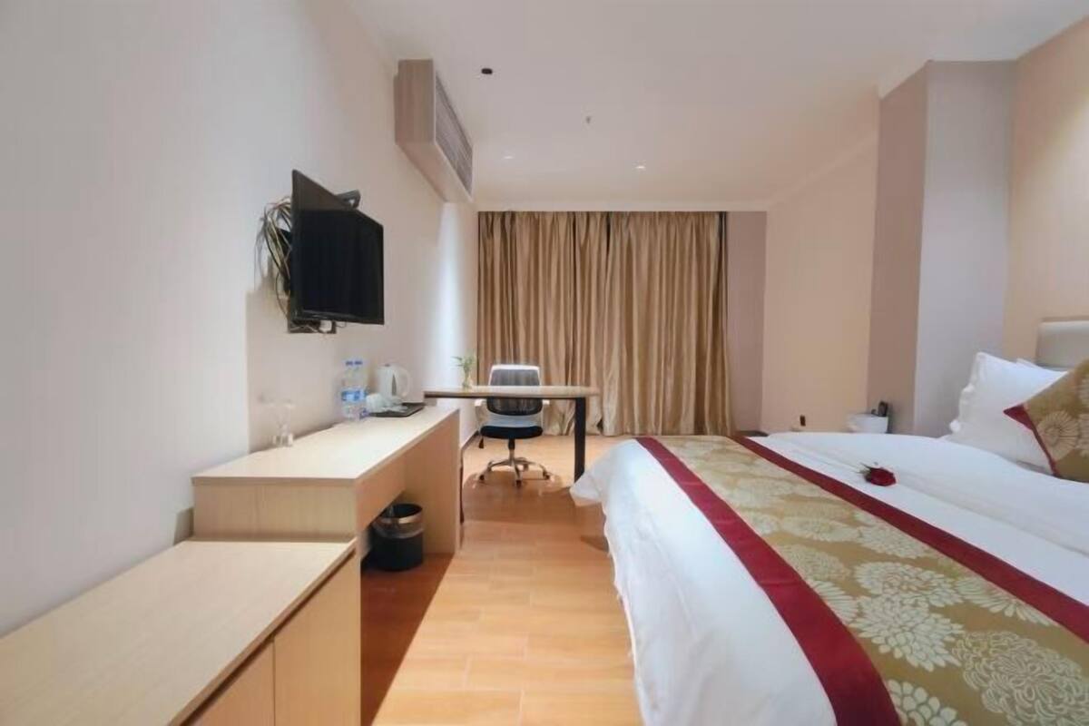 Ein Hotelzimmer mit Bett, Schreibtisch, Stuhl, Fernseher und Vorhang.