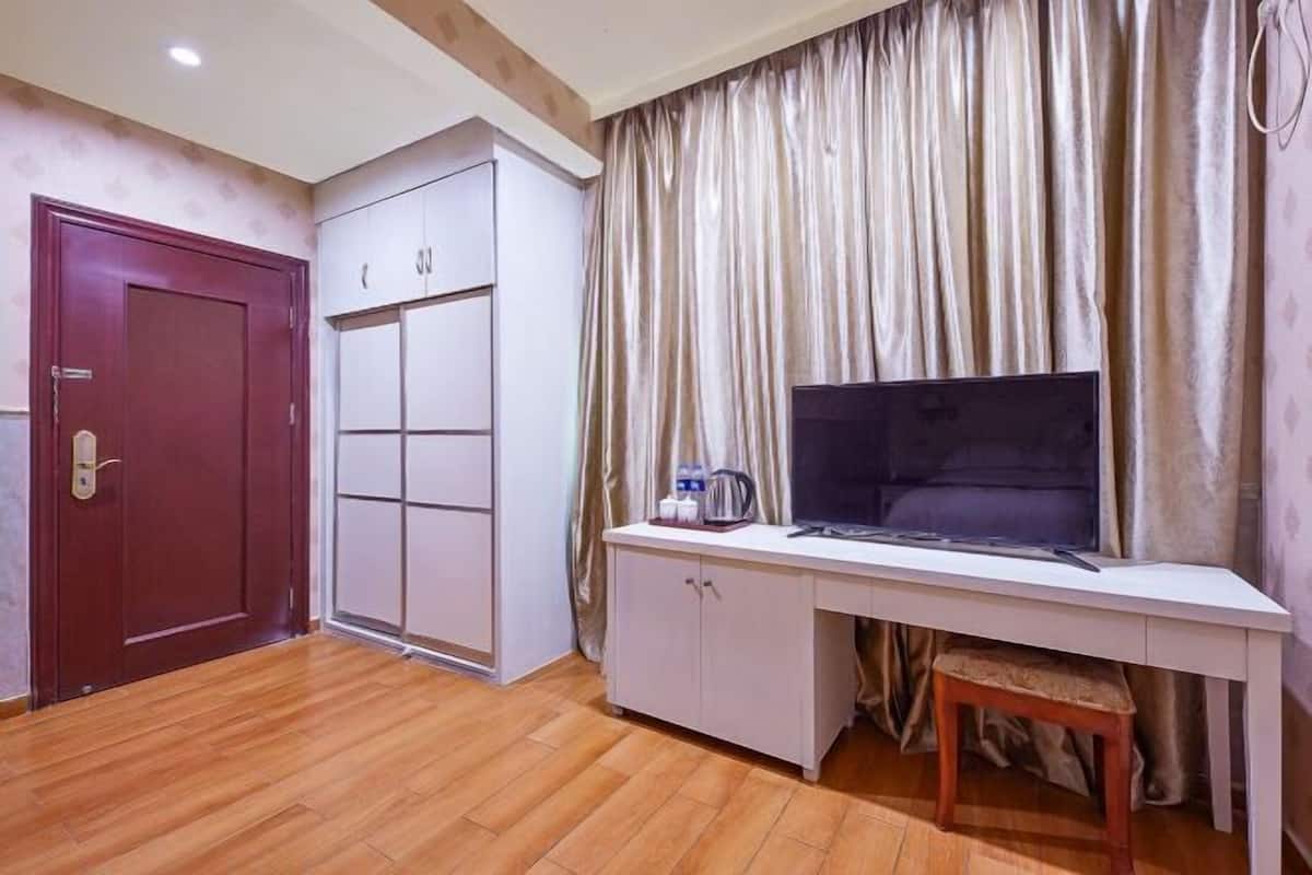 Ein Zimmer mit Holzboden, Schreibtisch mit Stuhl, Fernseher, Kleiderschrank und einer Tür.
