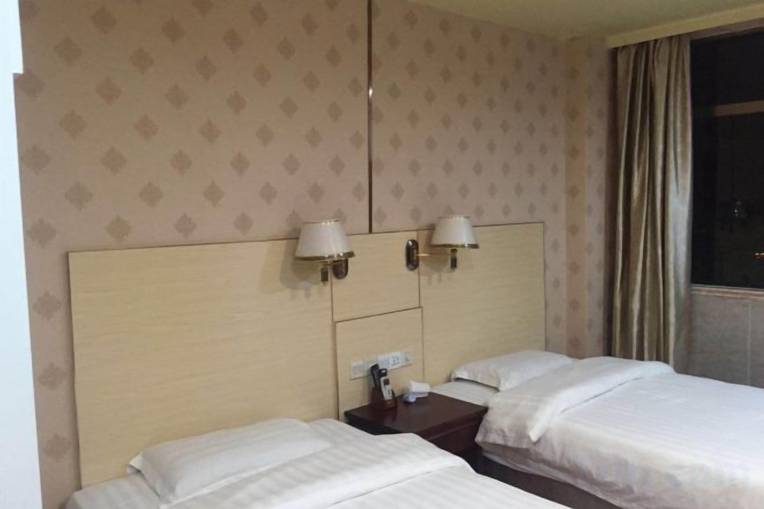 Une chambre d’hôtel avec deux lits, une tête de lit, des lampes fixées au mur et une fenêtre avec des rideaux.