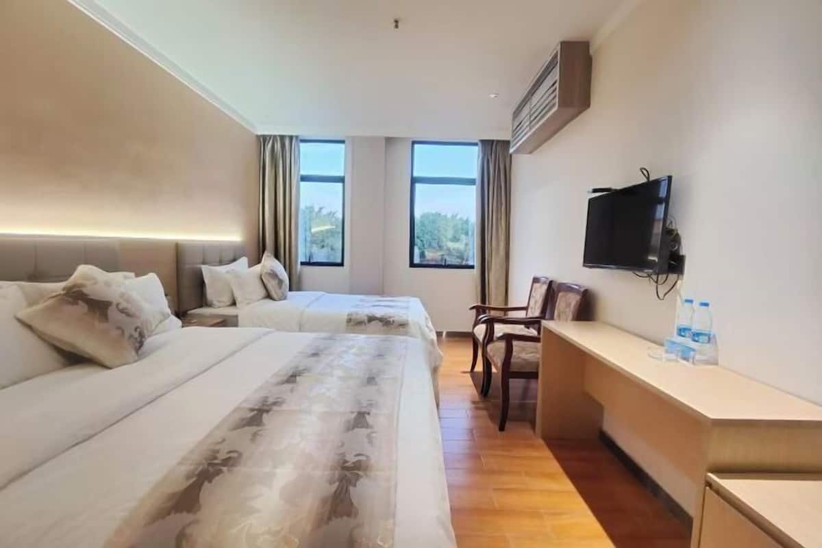 Ein Hotelzimmer mit zwei Betten, einem Schreibtisch, einem Sessel, einem Fernseher und großen Fenstern.