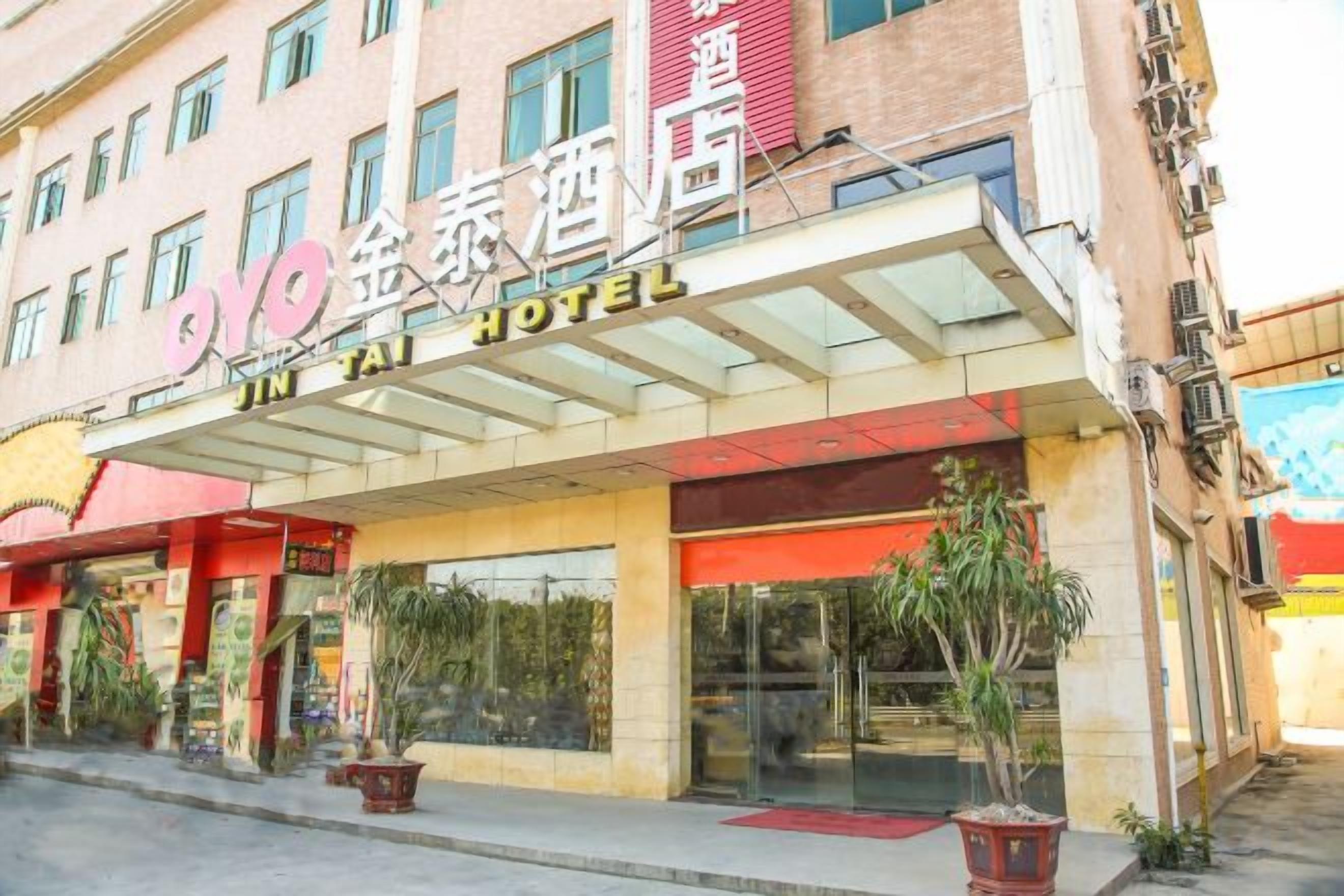 A hotel with a glass entrance, potted plants, and a sign with Chinese characters.