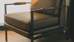 A modern chair with a high backrest and armrests, positioned on a wooden floor.