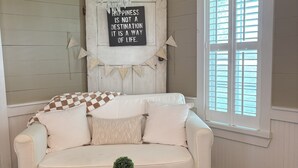 Une pièce chaleureuse avec un canapé blanc, une petite table sur laquelle est posée une plante, et un panneau décoratif accroché au mur.