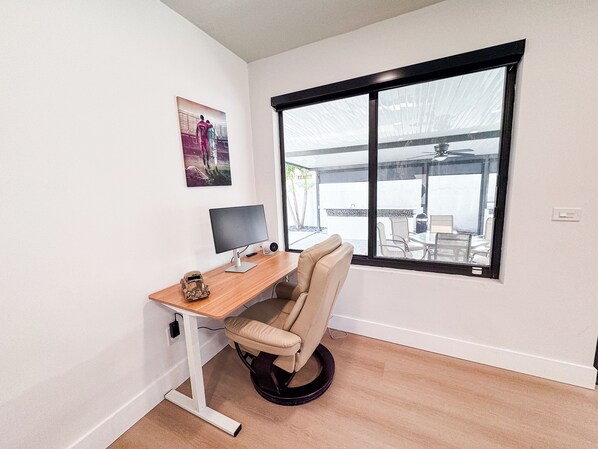 A modern office space with a desk, chair, computer, and a large window.