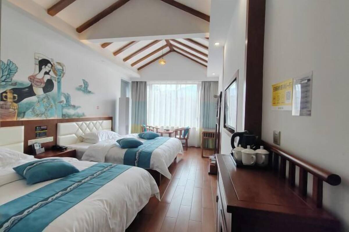 Une chambre d’hôtel avec deux lits, une fresque murale, un plafond en bois et une vue sur l’extérieur.