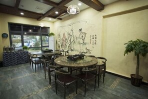 A dining area with round tables and chairs, a large window, and a mural on the wall. - Mengxiyuan Resort Hotel (Zhangjiajie)