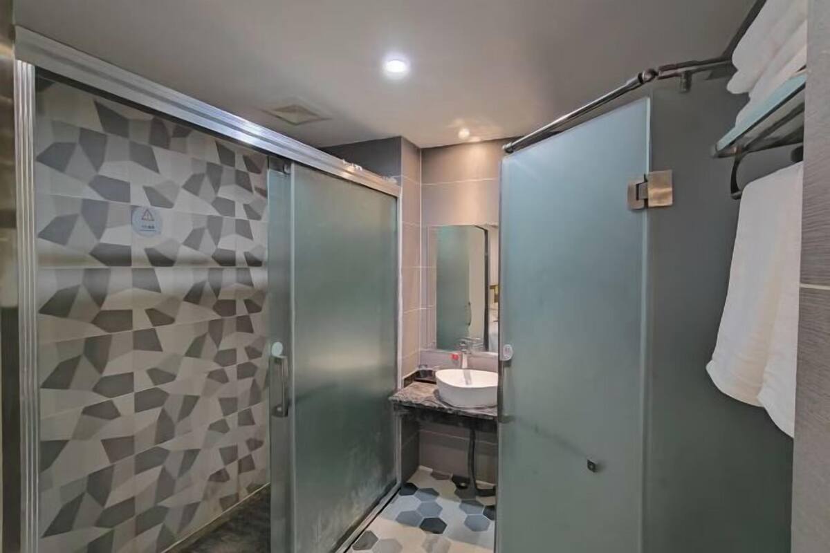 Une salle de bain moderne avec un mur de douche orné d’un motif géométrique, une douche à parois de verre, un lavabo avec un plan de toilette en marbre et un porte-serviettes.