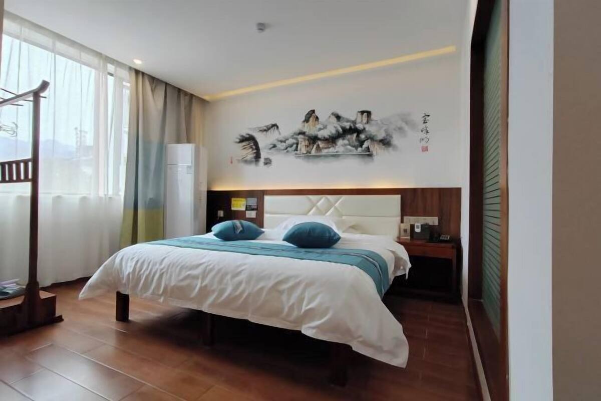 Une chambre d’hôtel avec un lit, une table de chevet, un tableau au mur et une fenêtre avec des rideaux.
