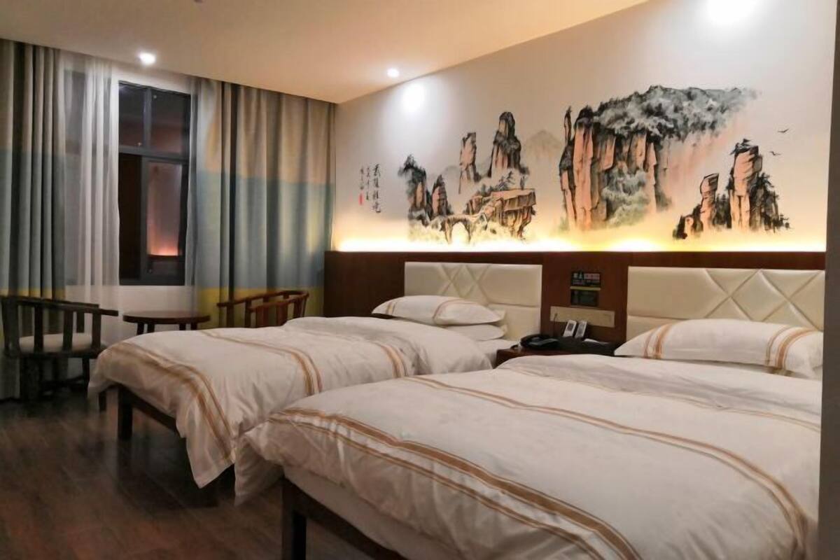 Une chambre d’hôtel avec deux lits, un bureau, une chaise, un grand tableau au mur et une fenêtre avec des rideaux.