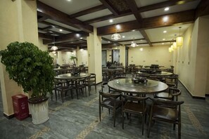 A spacious dining area with multiple round tables and chairs, a large potted plant, and a marble floor. - Mengxiyuan Resort Hotel (Zhangjiajie)