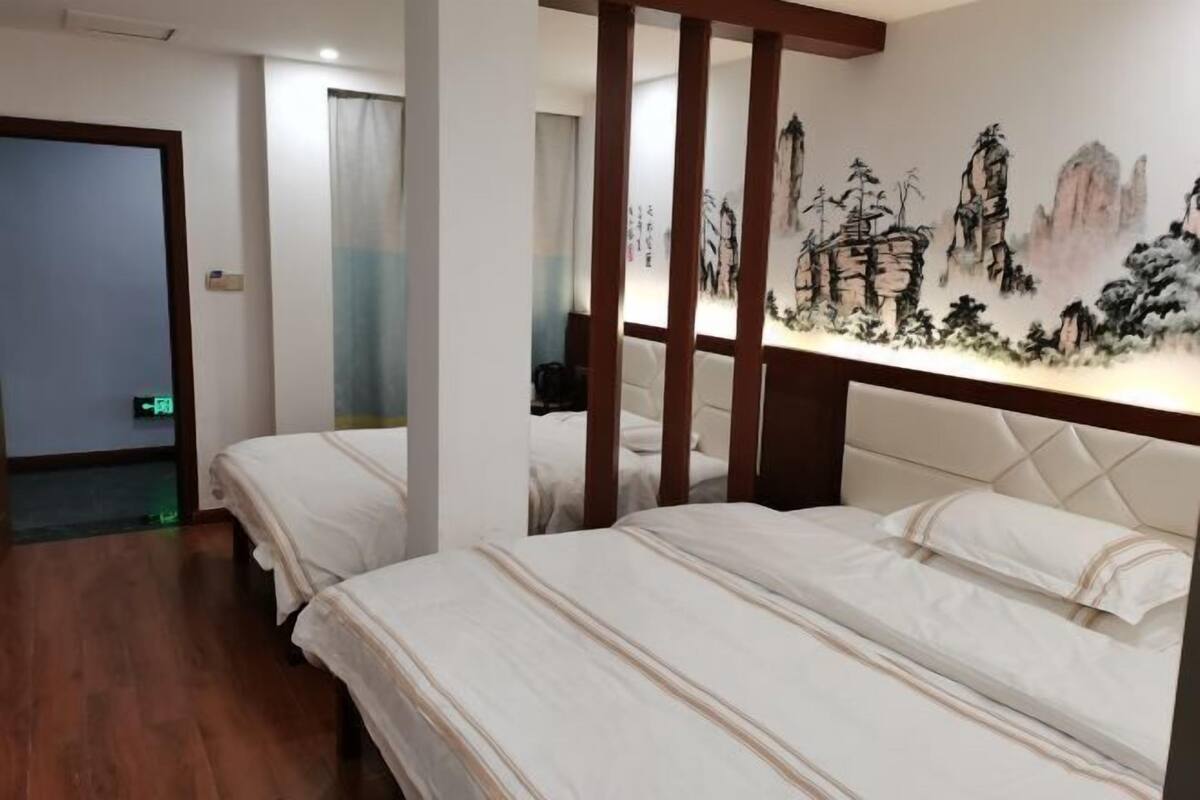 Une chambre d’hôtel avec deux lits, une tête de lit en bois, un tableau au mur et une porte.