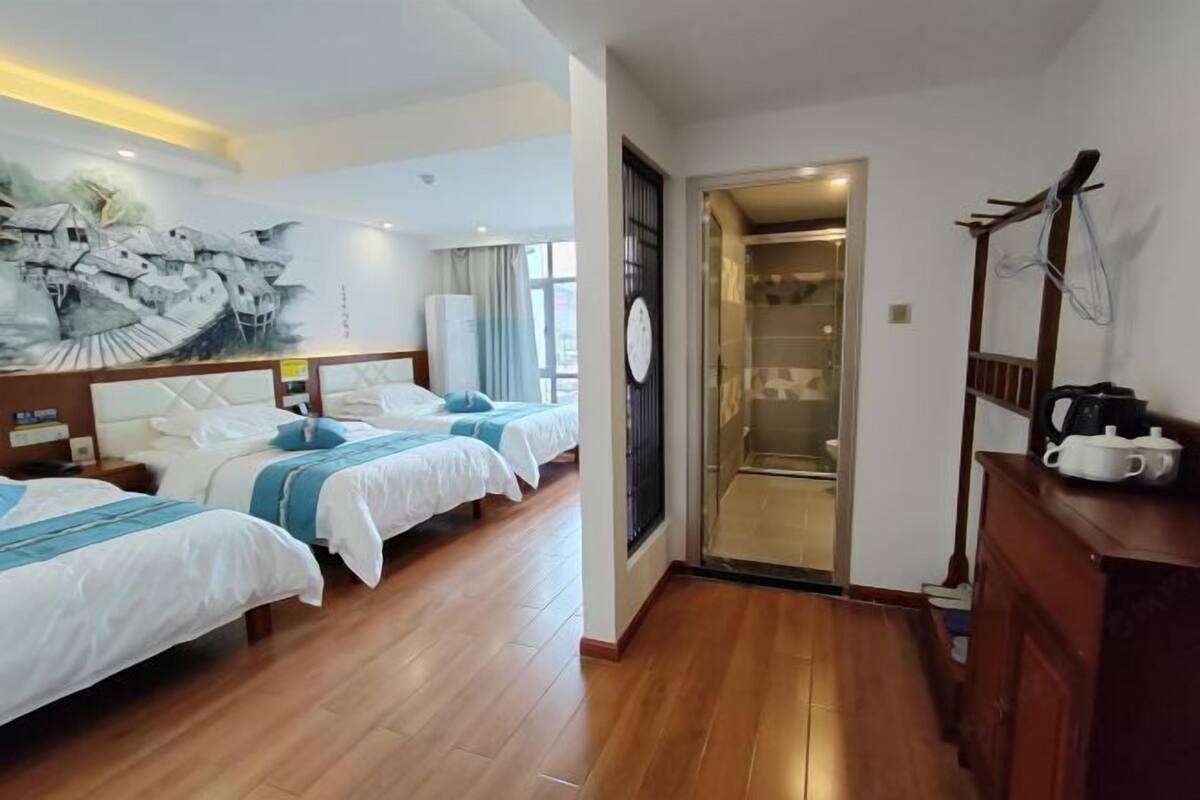 Une chambre d’hôtel avec deux lits, un plancher en bois, une fresque murale, une horloge et une salle de bain avec une porte en verre.