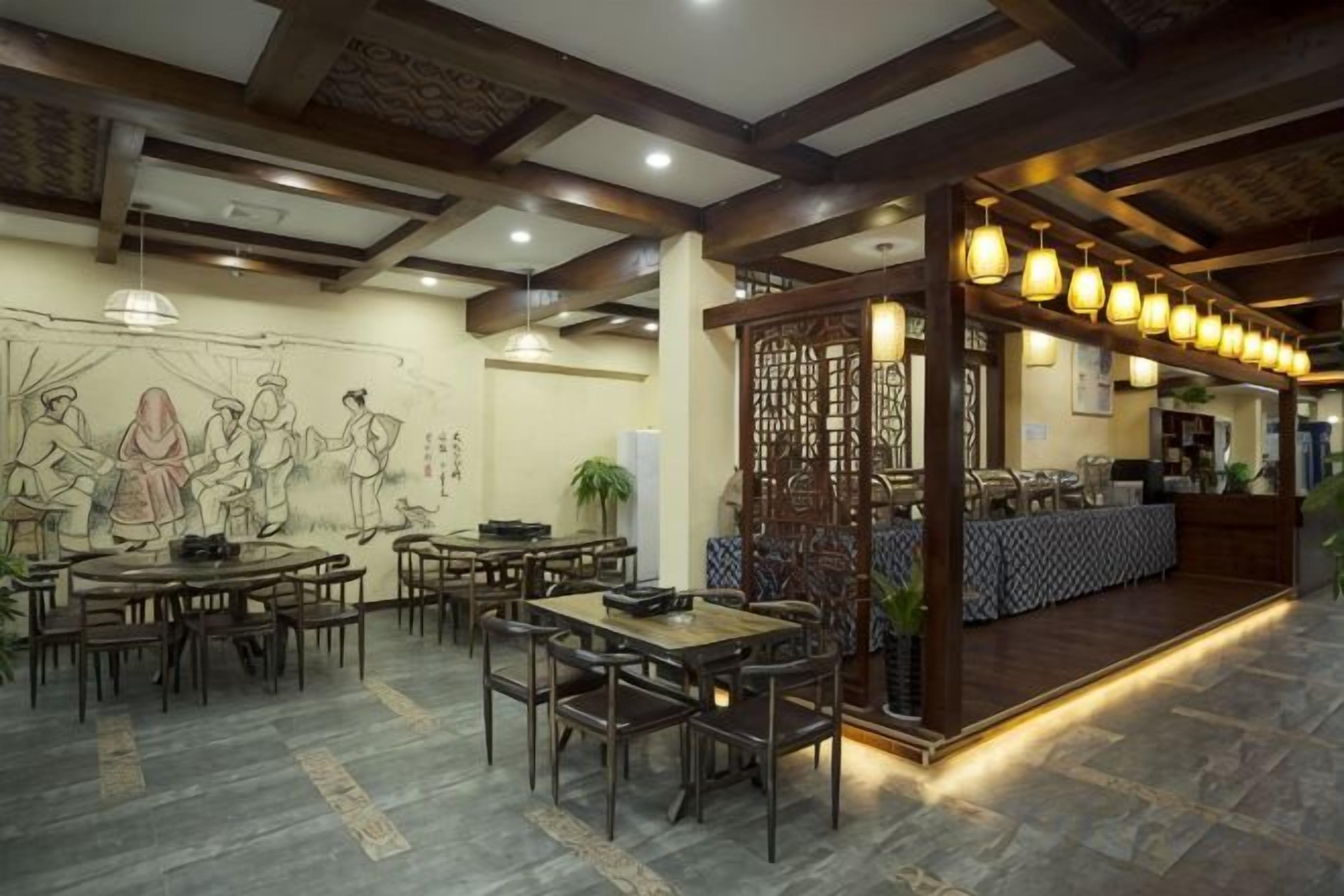 Un restaurant avec des tables et des chaises rondes, un comptoir recouvert d’une nappe à motifs et un mur décoratif orné d’une fresque.