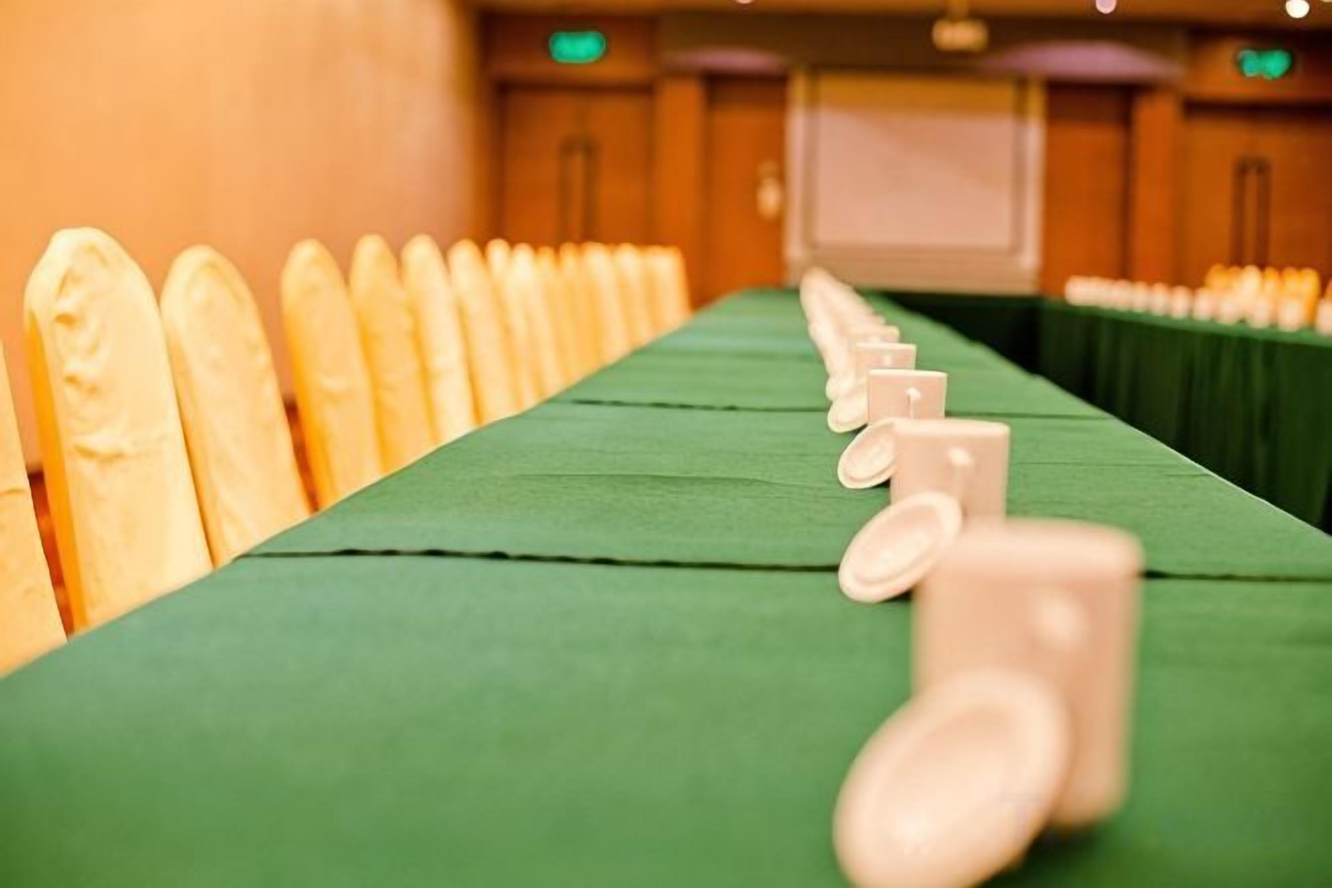 A long table with chairs lined up on one side, a green tablecloth, and a projector screen in the background.