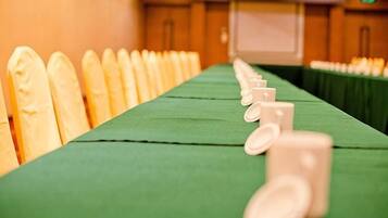 A long table with chairs lined up on one side, a green tablecloth, and a projector screen in the background.