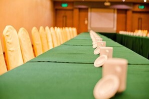 Ein langer Tisch mit Stühlen an einer Seite, eine grüne Tischdecke und im Hintergrund eine Projektionsleinwand.
