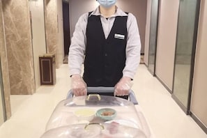 Un empleado de hotel empuja un carrito con una mesa cubierta que contiene alimentos.