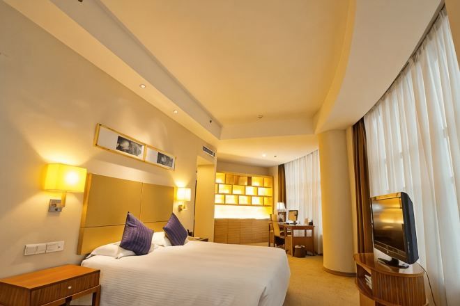 A hotel room with a large bed, bedside tables, a TV, and a desk with a chair.