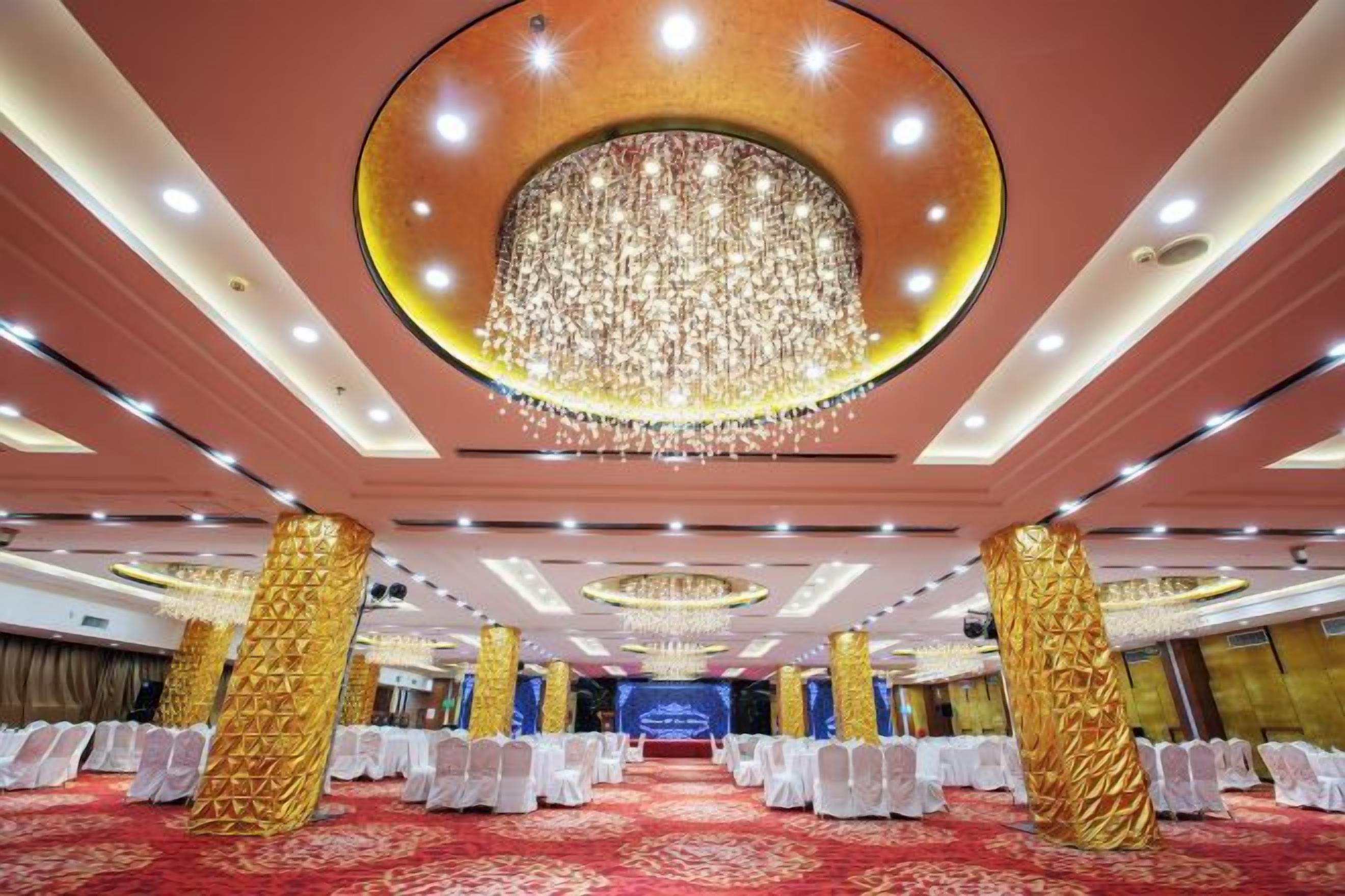 A banquet hall with rows of white chairs, a large chandelier, and a red carpet.