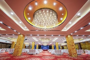 A banquet hall with rows of white chairs, a large chandelier, and a red carpet.