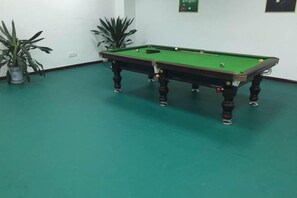 A pool table in a room with green flooring and potted plants.