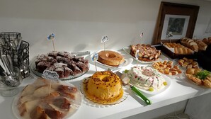 Una mesa de buffet con diversos postres y pasteles, incluyendo un pastel decorado con una motocicleta, un postre amarillo con lunares rojos y varios tipos de pan.