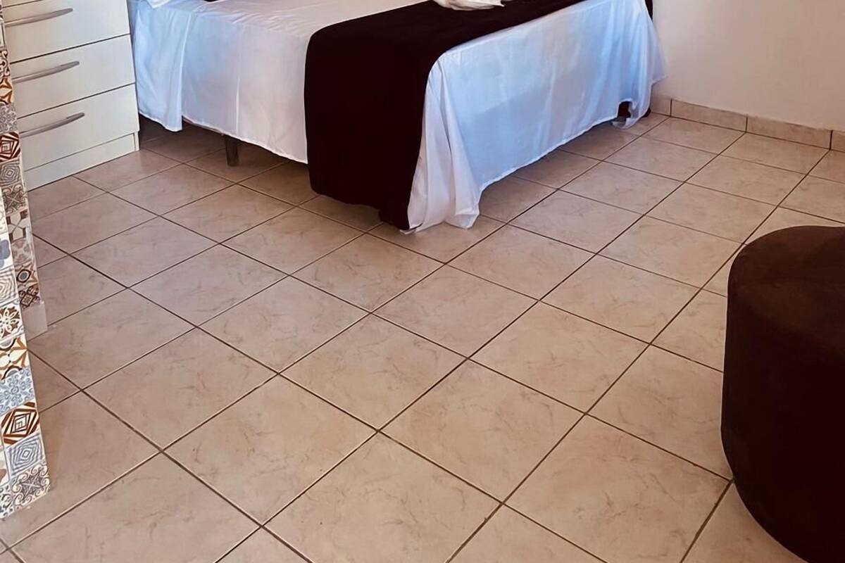 Una cama bien hecha con ropa de cama blanca y negra, una mesita de noche con toallas y un armario blanco con espejo.