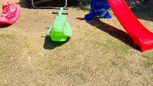Un parque infantil con un trampolín, un tobogán y una pequeña estructura de juego verde.