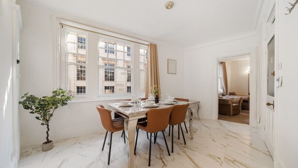 A dining area with a marble floor, white walls, and a large window with curtains. - 3 Bedroom Apartment Steps from Piccadilly Circus! (London)