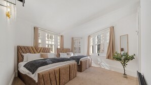 A bedroom with two beds, large windows, a mirror, and a small plant. - 3 Bedroom Apartment Steps from Piccadilly Circus! (London)
