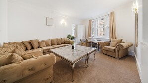 A spacious living room with a beige sectional sofa, a coffee table, and a small side table. - 3 Bedroom Apartment Steps from Piccadilly Circus! (London)