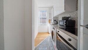 A modern kitchen with a washing machine, microwave, and stove. - Stylish & Bright Studio in the Heart of Soho 8 (London)