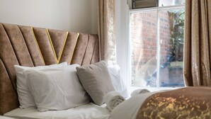Een opgemaakt bed met hoofdbord, kussens en dekbed.
