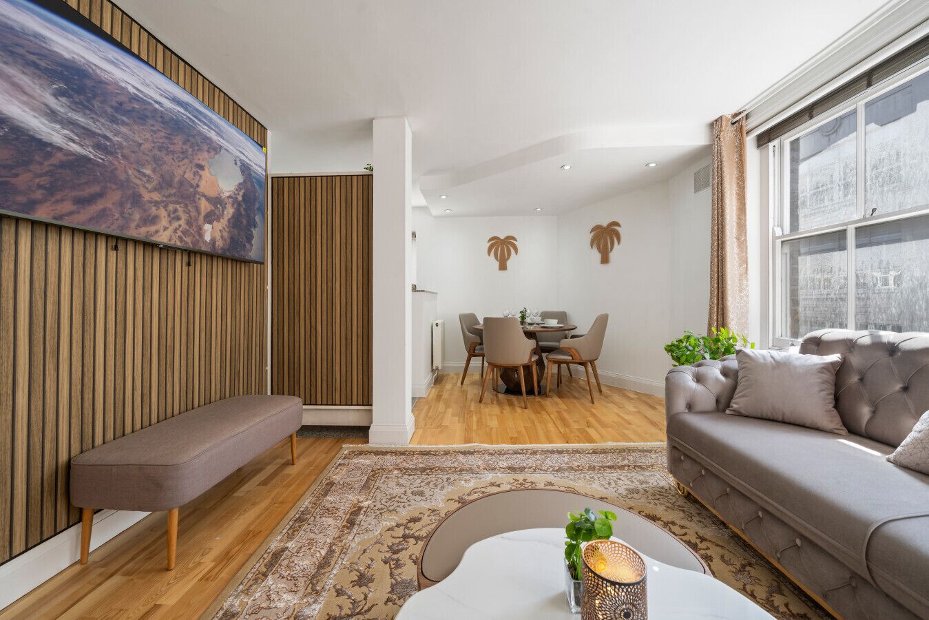 Ein modernes Wohnzimmer mit einer Couch, einer Bank, einem Esstisch mit Stühlen und einem großen Gemälde an der Wand.