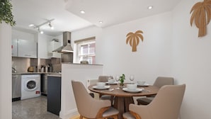 Una cocina compacta con electrodomésticos modernos, un comedor con una mesa redonda y cuatro sillas, y una palmera decorativa en la pared.