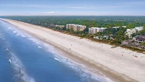 Ein Strand mit einem weiten Sandstreifen, einigen Gebäuden und einem bewaldeten Gebiet im Hintergrund.