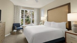 Ein Hotelzimmer mit einem großen Bett, einem Schreibtisch, einem Sessel, einem Fenster mit Vorhängen und einem Fernseher.