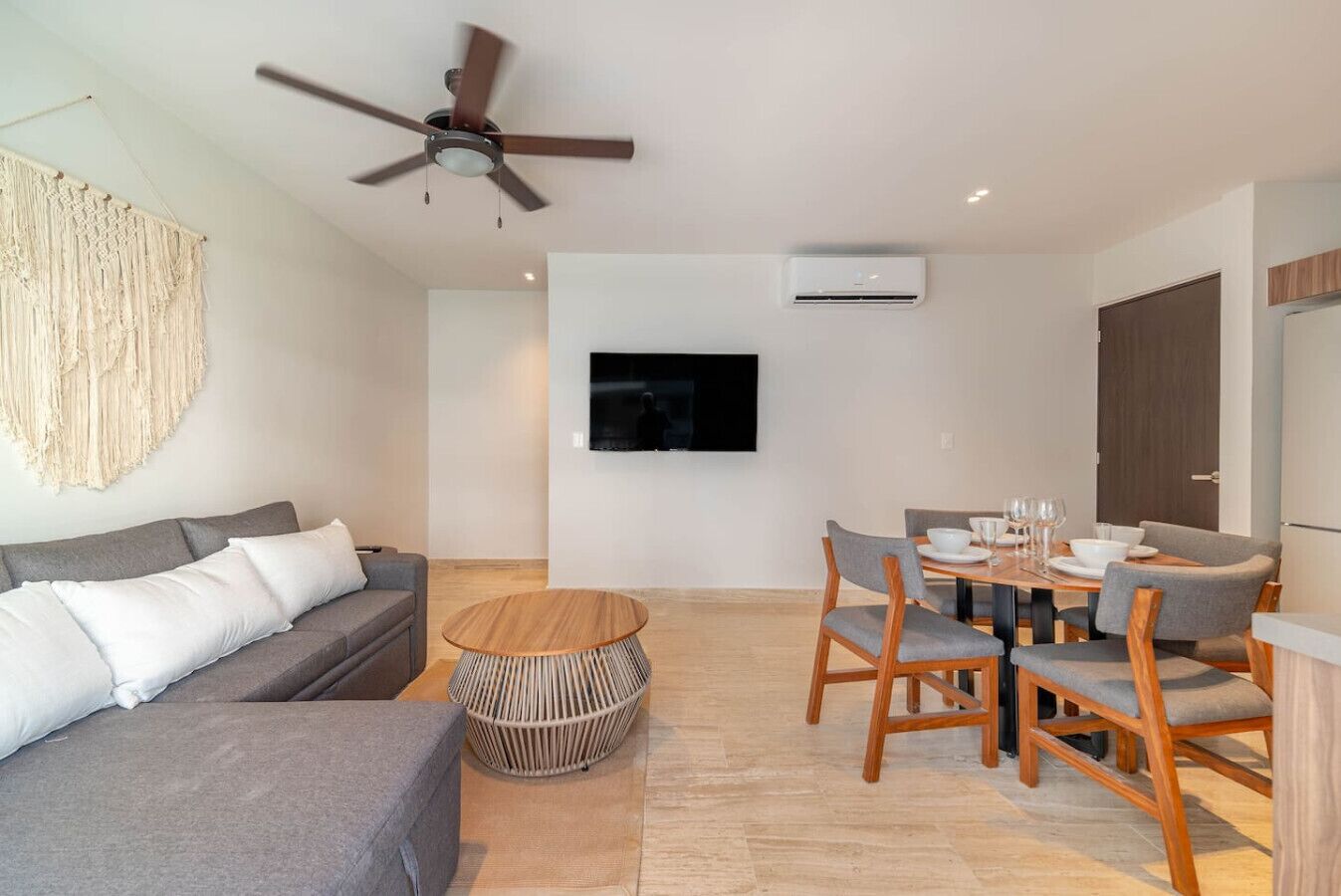 A modern living room with a grey sofa, a round wooden coffee table, and a dining area with a wooden table and chairs.