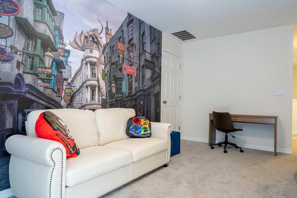A room with a white leather sofa, a colorful pillow, a wooden desk, and a wall mural of a city street. - Family Fun Moana Mario Harry Potter Stay (Kissimmee)