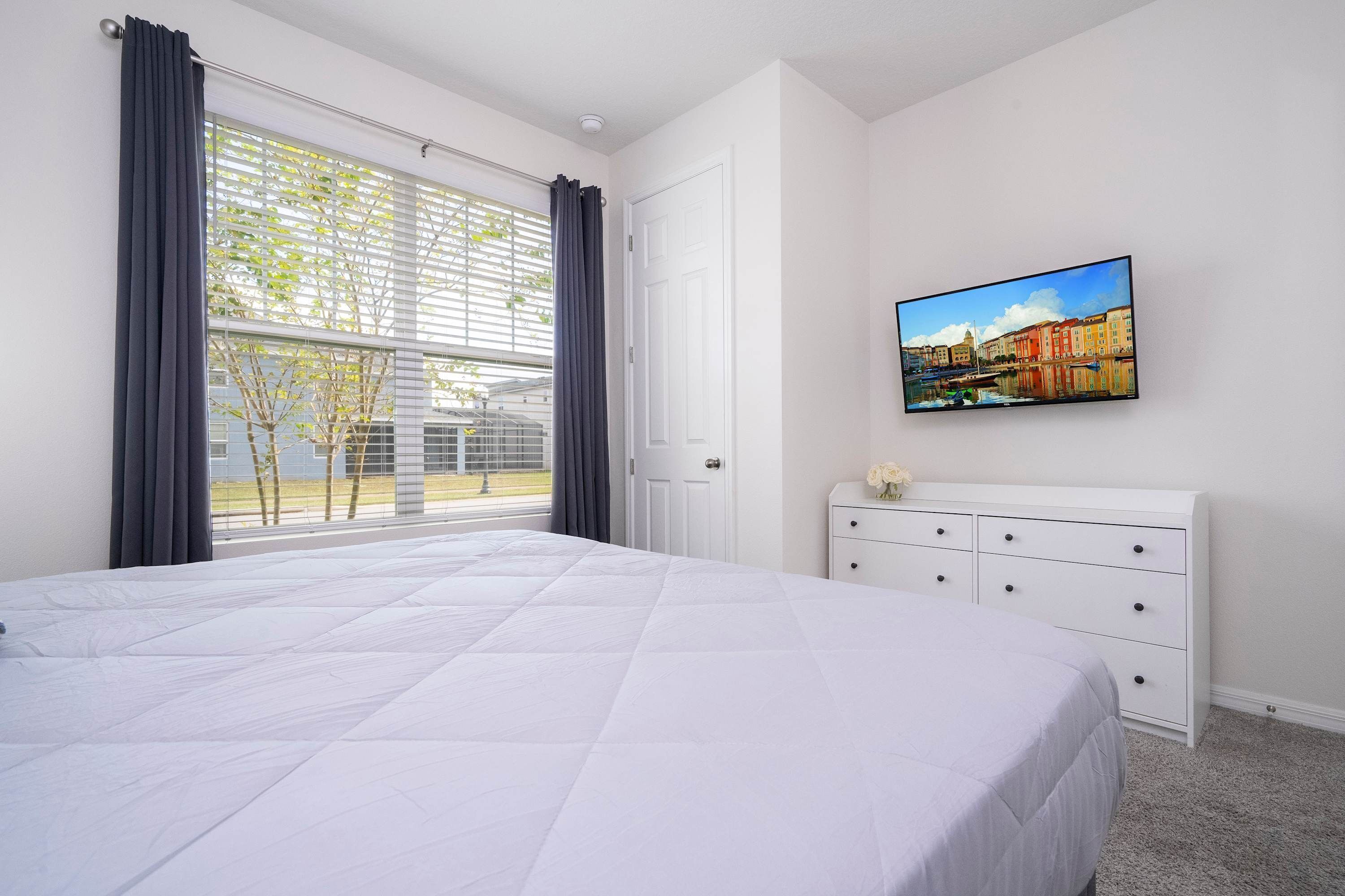 Ein Schlafzimmer mit einem großen Bett, einem Schminktisch, einem Gemälde und einem Fenster mit Vorhängen.