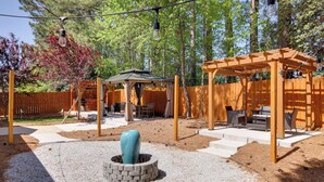Ein Garten mit einer Holz-Pergola, einem Pavillon und einer Feuerstelle.