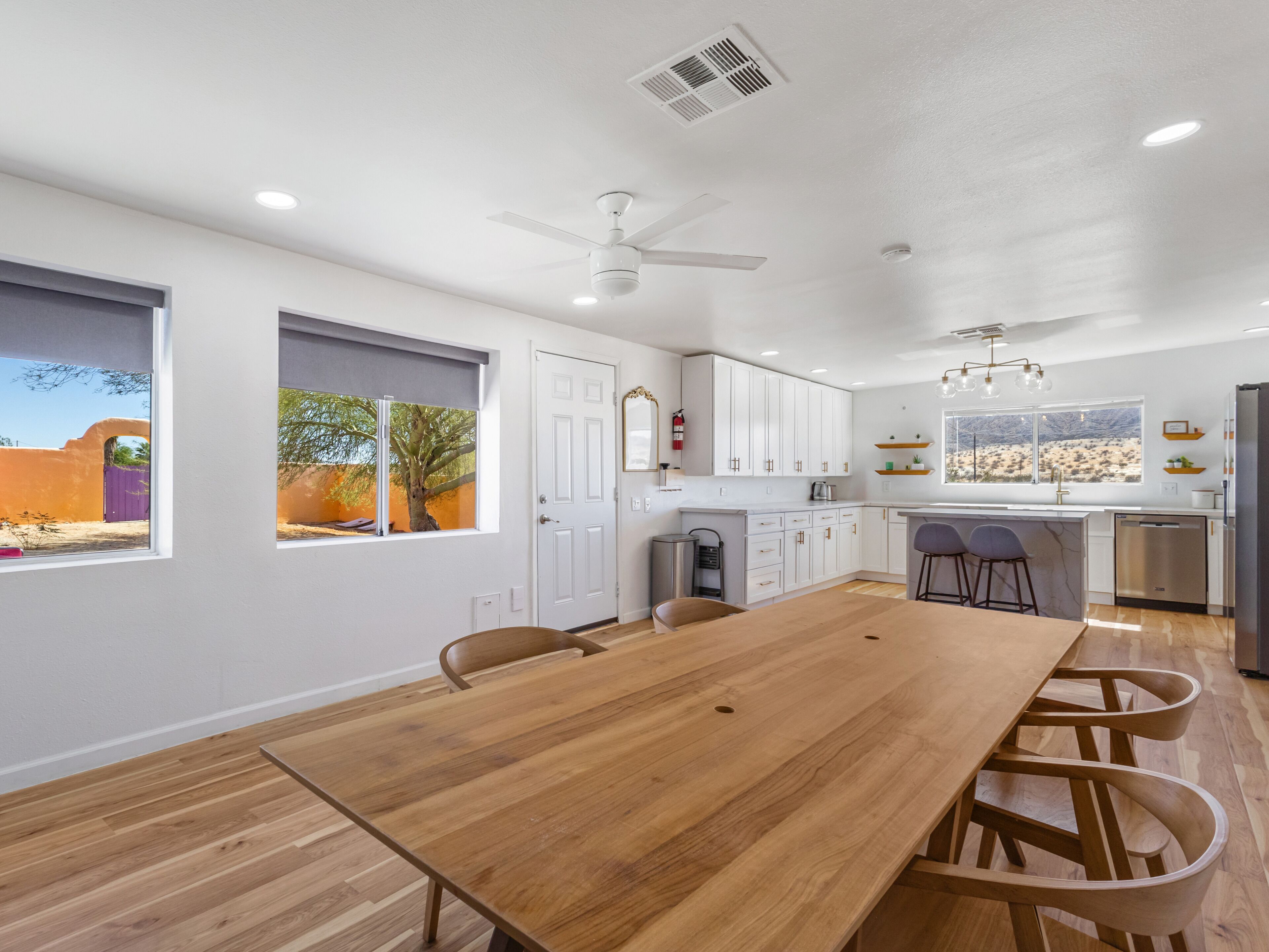 A modern kitchen with white cabinets, a wooden dining table, and a view of a desert landscape.