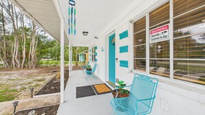 A porch with a blue chair and a potted plant, a warning sign about security cameras, and a view of the surrounding area.