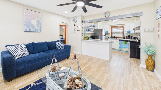 A modern living room with a blue sofa, a glass coffee table, and a ceiling fan.