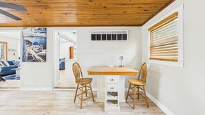 A room with a wooden ceiling, a white wall with a calendar, a wooden table with two chairs, and a door leading to another room.