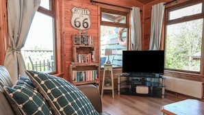 A cozy cabin interior with a sofa, a bookshelf, a television, and a sign reading "Route 66". - The Beach House (Ilfracombe)