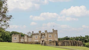 A castle with a large lawn in front, a stone wall, and a clear sky. - The Beach House (Ilfracombe)